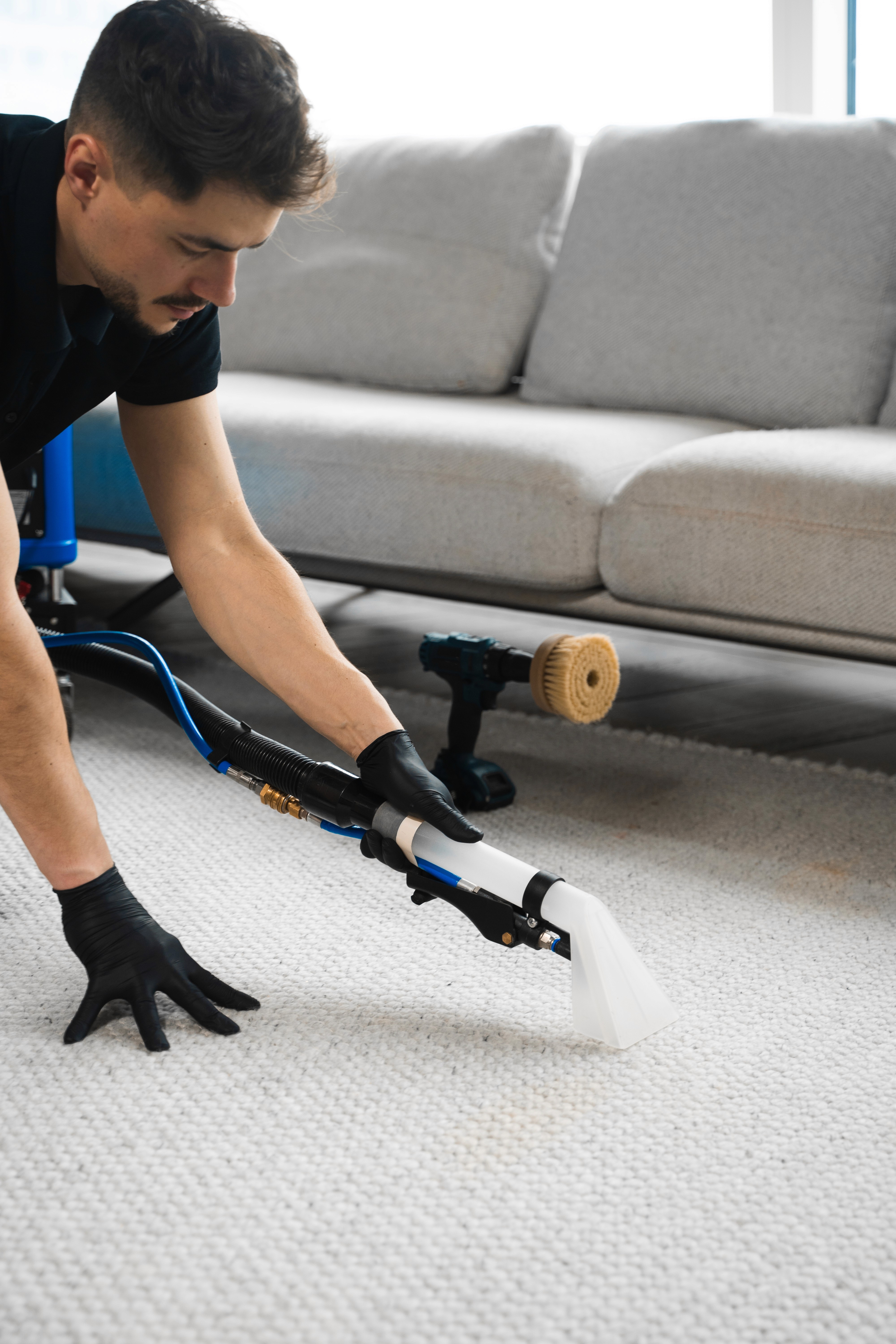 Cleaner using a carpet cleaning tool near a sofa
